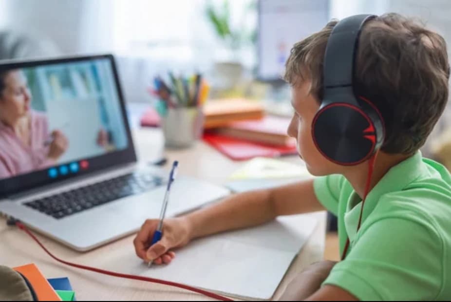 A student wearing headphones and writing notes during an online lesson