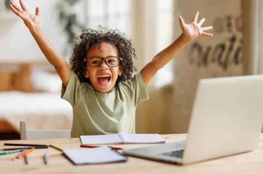 A child celebrating a learning breakthrough at a desk with a laptop